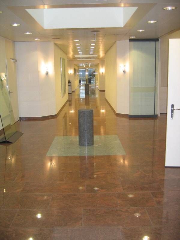 Ein breiter Flur mit polierten braunen Steinböden, weissen Wänden, eingelassenen Deckenleuchten und einer zentralen zylindrischen Säule.