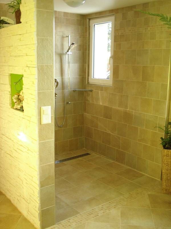 Eine begehbare Dusche mit hellbraun gefliesten Wänden, einem bodenebenen Linienablauf, einem verchromten Duschkopf und einer eingelassenen Wandnische.