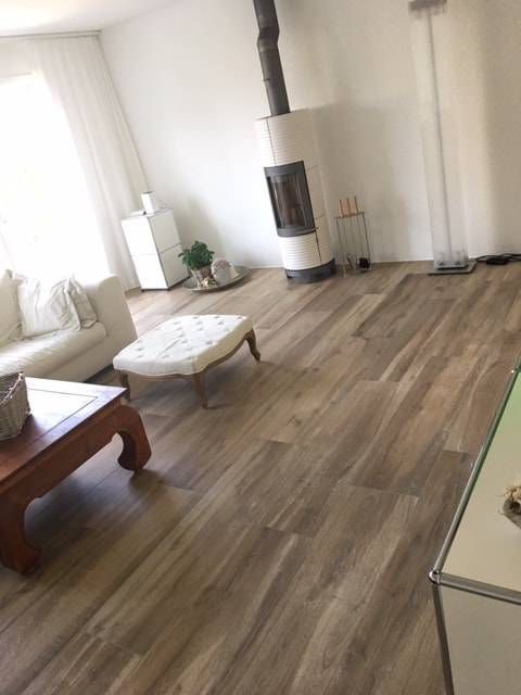 Ein modernes Wohnzimmer mit Holzboden, einem weissen Sofa, einem gepolsterten Hocker, einem Couchtisch aus Holz und einem zylindrischen Kamin.