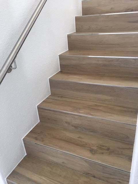 Eine Treppe mit Holzstufen und einem Metallgeländer, die an einer weissen Wand befestigt ist.