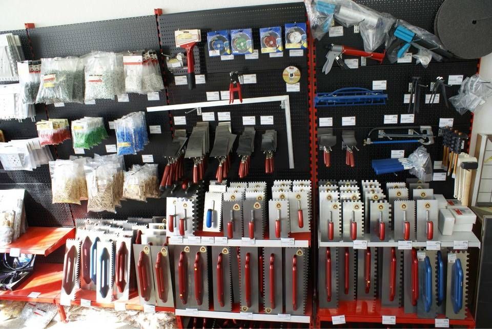 Eine Verkaufsfläche für Bau- und Maurerwerkzeuge, darunter Kellen, Sägen und Kunststoffzubehör auf Regalen mit Haken.