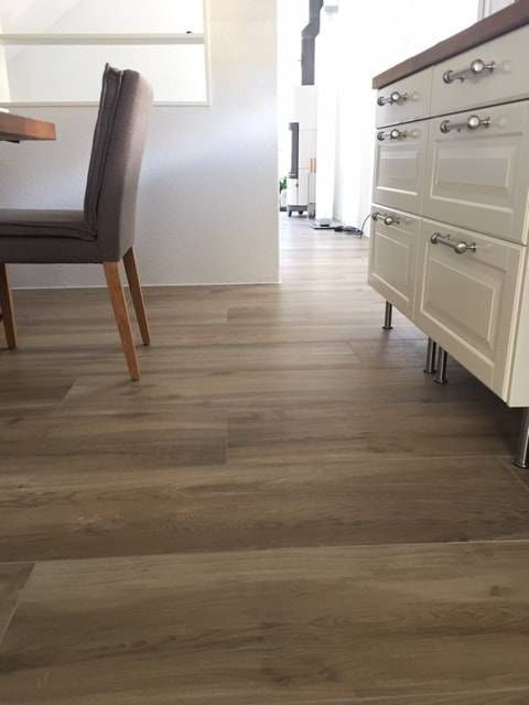 Ein modernes Interieur mit hellen Holzdielen, die zu einem Flur führen, daneben ein Esszimmerstuhl und weisse Schränke.