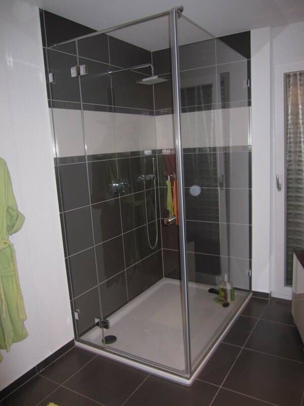 Eine moderne, ebenerdige Dusche mit Glasabtrennung, weißer Duschwanne und dunkel gefliesten Wänden mit einem horizontalen weißen Streifen.