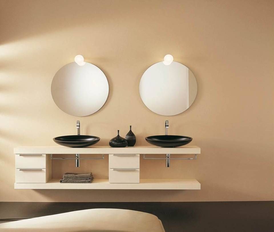 Ein minimalistischer Doppelwaschtisch mit zwei schwarzen Aufsatzwaschbecken und runden Spiegeln an einer warmen beigefarbenen Wand.