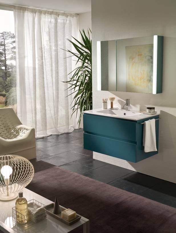 Ein türkisfarbener, wandmontierter Waschtisch mit weißem Waschbecken und beleuchtetem Spiegel in einem modernen, mit Pflanzen gefüllten Badezimmer.