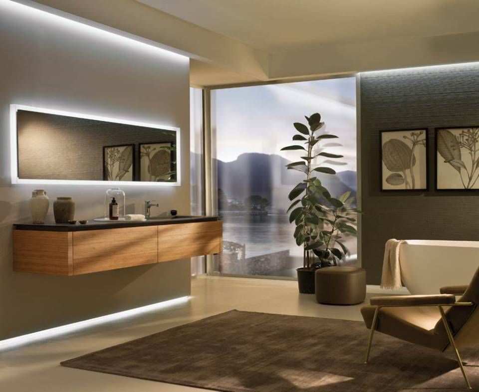 Ein luxuriöses Badezimmer mit einem schwebenden Waschtisch aus Holz, einem beleuchteten Spiegel, einer Pflanze und Blick auf die Berge durch ein Fenster.