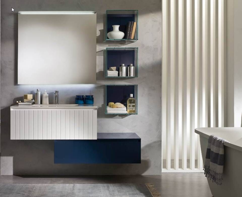 Ein moderner Badezimmerwaschtisch mit weißem, geriffeltem Schrank, marineblauer Schublade, wandmontierten Regalen und einem großen, beleuchteten Spiegel.