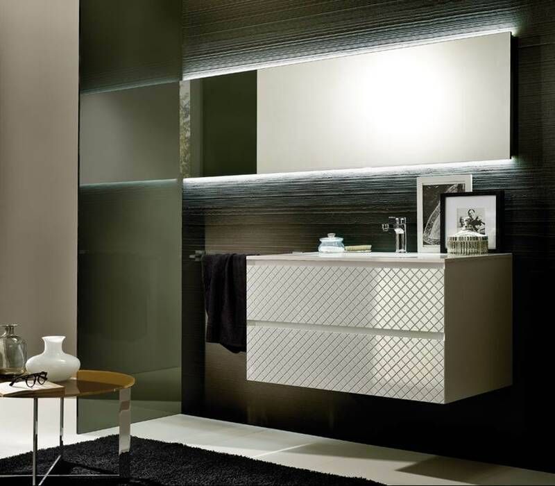 Ein moderner Waschtisch mit strukturierten weißen Schubladen, der an einer dunklen, horizontal gerippten Wand unter einem beleuchteten Spiegel angebracht ist.