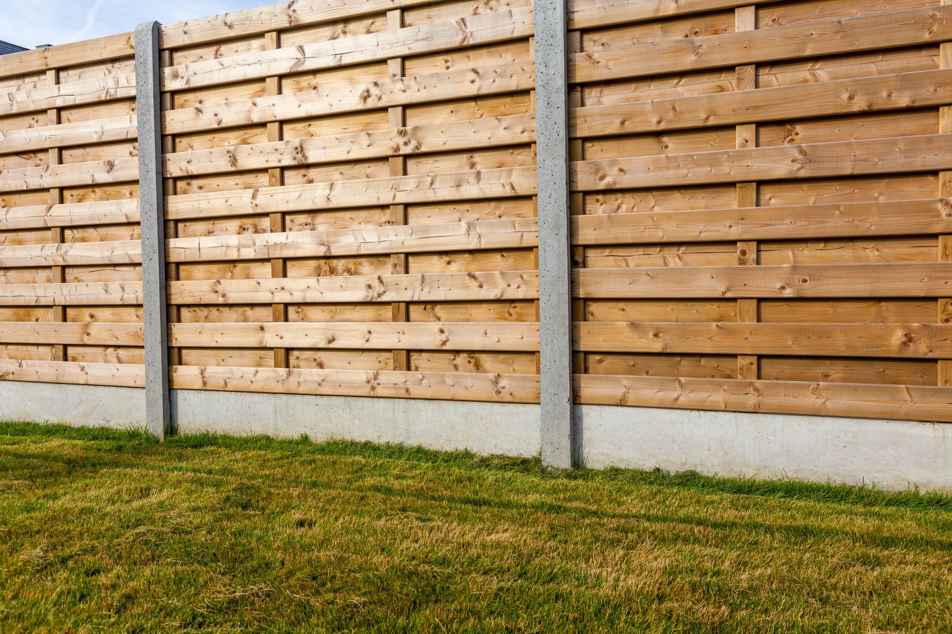 Une clôture en bois composée de planches horizontales et de poteaux en béton.