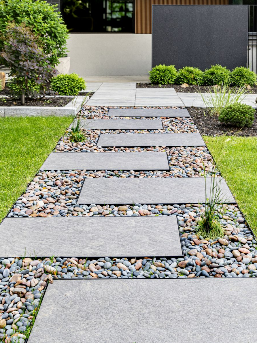 Un chemin de dalles rectangulaires en pierre grise, incrustées de galets décoratifs dans un jardin.