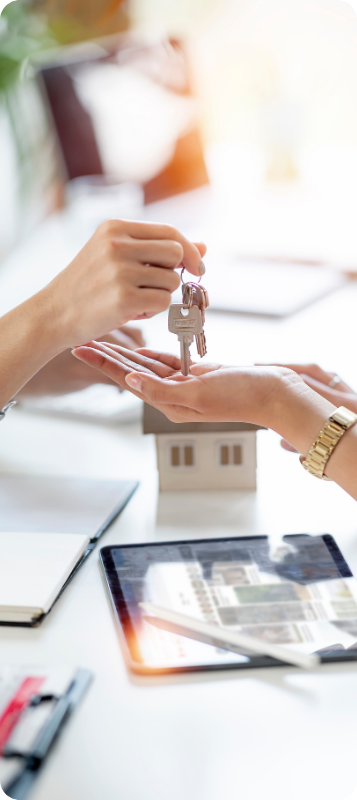 Une main donne les clés d'une maison à une autre, devant une maquette de maison. Transaction immobilière.