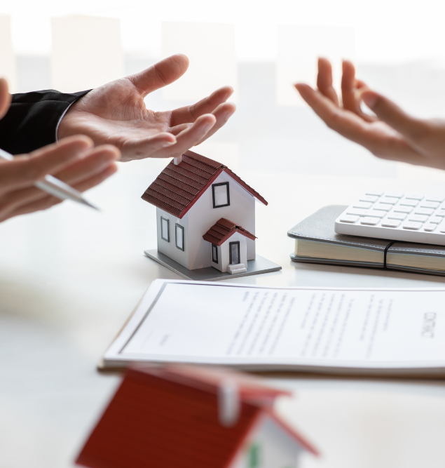 Des mains gesticulant au-dessus d'une table avec une maison modèle, des documents et une calculatrice