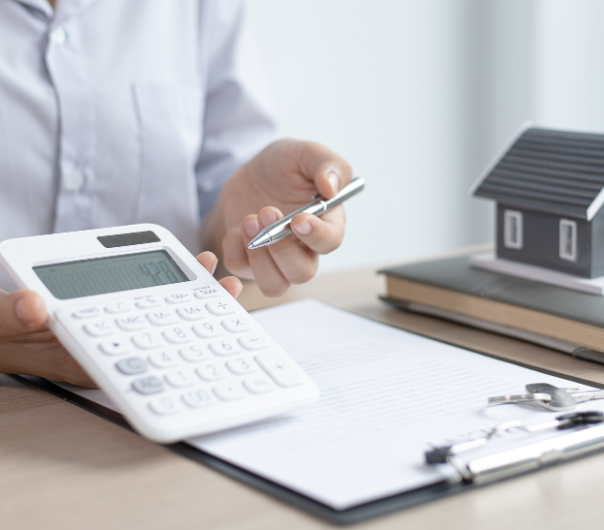 Personne calculant avec une calculatrice, un modèle de maison et des papiers.