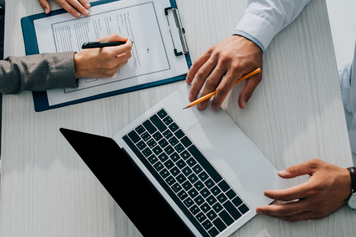 Mains écrivant sur un presse-papiers et utilisant un ordinateur portable sur une table.