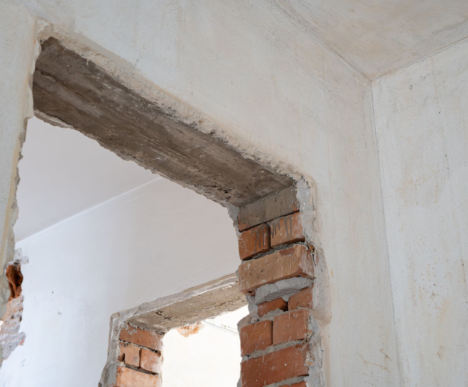 Une scène de construction montrant deux portes en briques inachevées avec des linteaux en béton apparents à l'intérieur d'une pièce aux murs plâtrés.