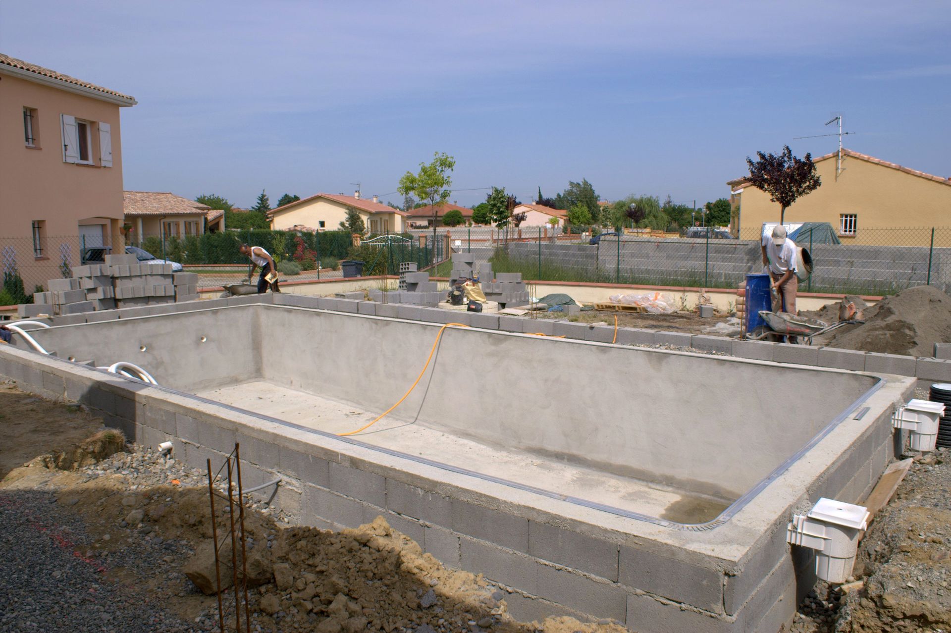 Un chantier de construction extérieur montrant la construction d'une coque de piscine rectangulaire en béton, avec des ouvriers à proximité.