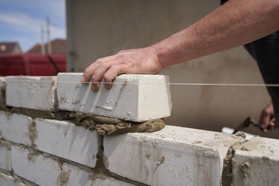Gros plan sur une main posant une brique blanche sur un lit de mortier, le long d'un fil de guidage, pour un projet de construction.