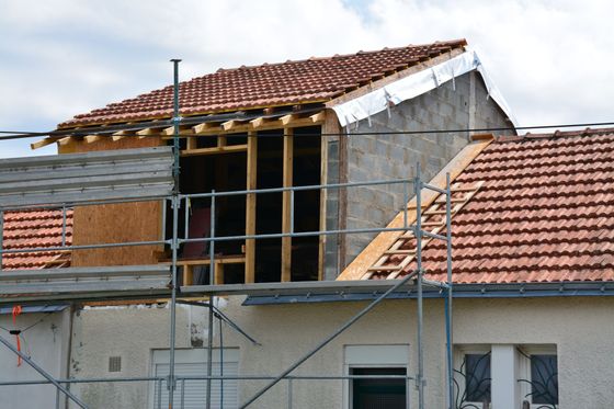 Une maison en construction avec une nouvelle ossature bois et une toiture en tuiles, entourée d'échafaudages métalliques.