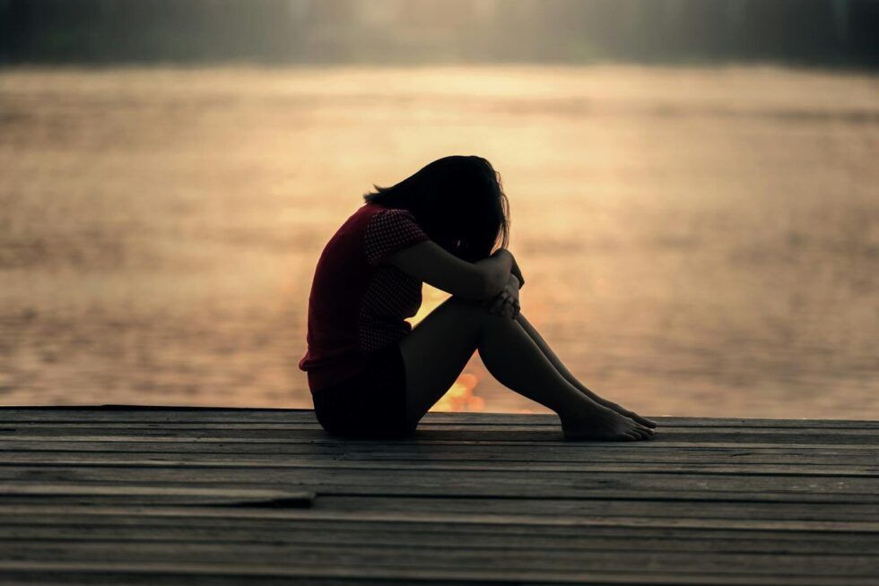 a girl sitting on a dock at sunset with her knees drawn to her chest, symbolising the quiet experience of feeling misunderstood as a neurodivergent person