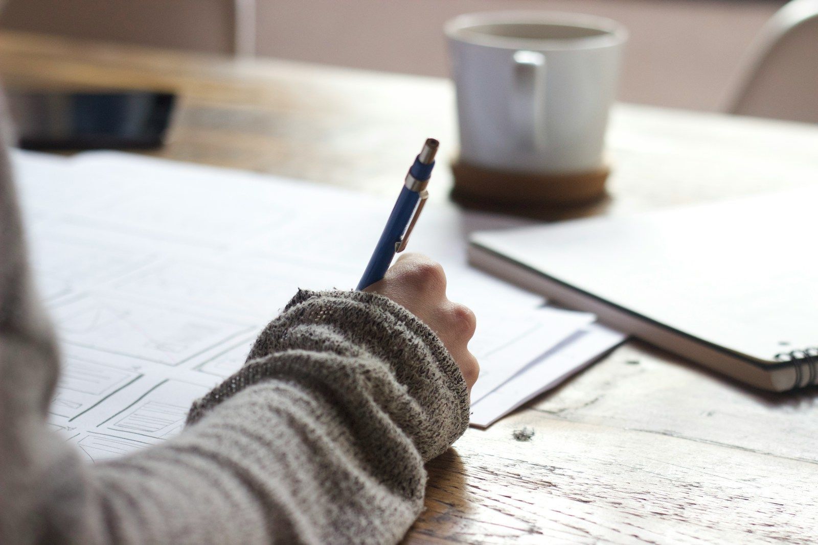 person writing in a notebook at a wooden table with a coffee mug, capturing the process of understanding ADHD