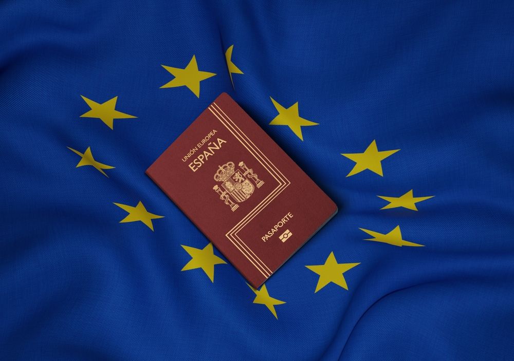 Un pasaporte español color burdeos colocado sobre una bandera azul de la Unión Europea.