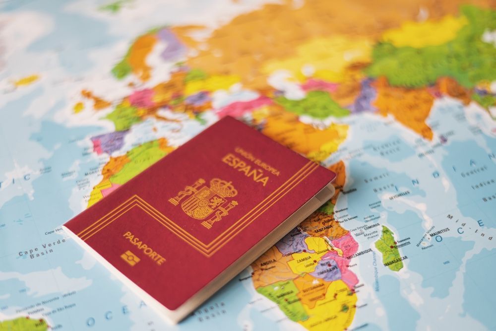 Un pasaporte español rojo reposa sobre un colorido mapamundi.
