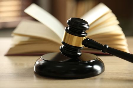 Un mazo de juez de madera descansa sobre su bloque de resonancia frente a un libro abierto sobre un escritorio.