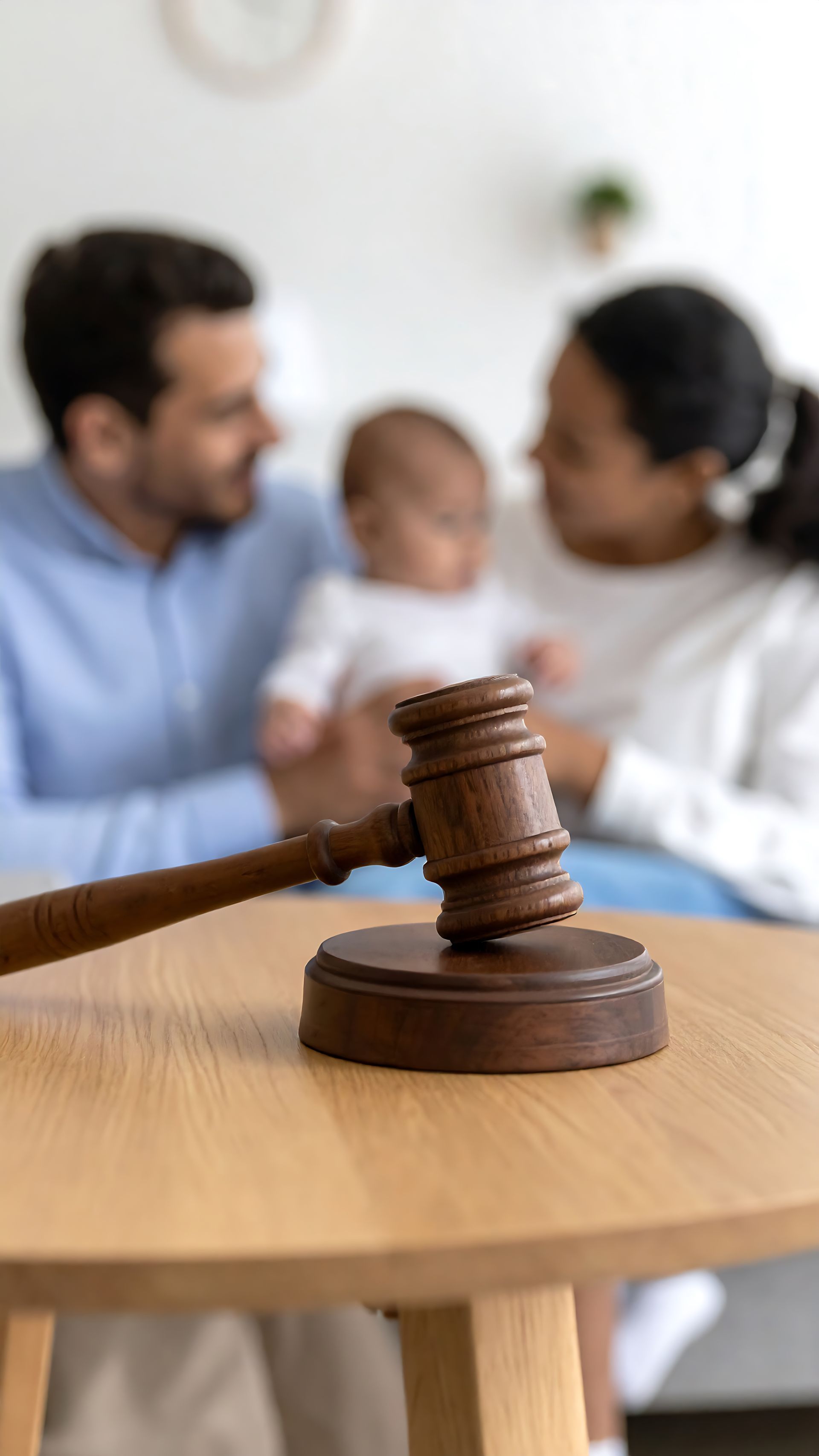 Marteau en bois sur la table ; famille floue avec bébé en arrière-plan.