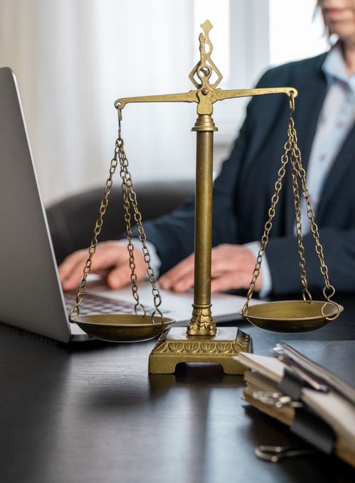 Balance de justice dorée sur un bureau, personne utilisant un ordinateur portable en arrière-plan.