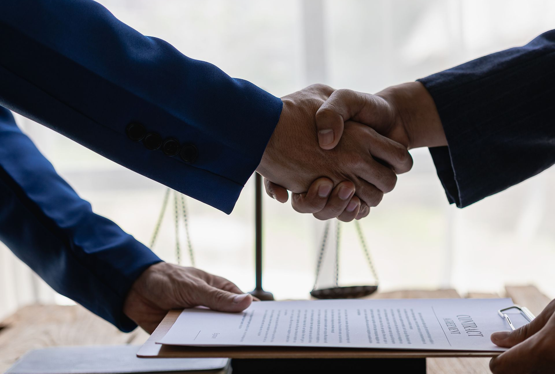 Deux personnes se serrant la main au sujet d'un contrat, la balance de la justice en arrière-plan.
