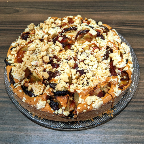Ein Kuchen liegt auf einem Glasteller auf einem Holztisch.