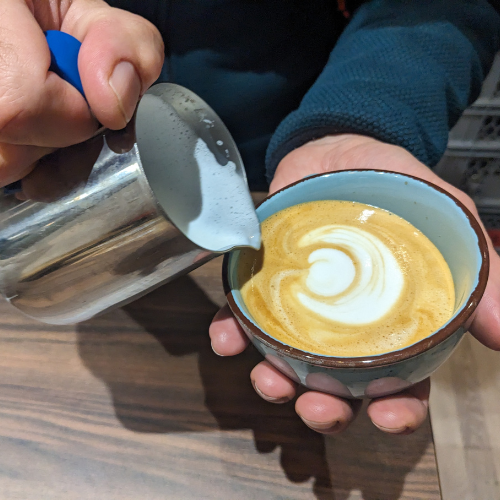 Eine Person gießt Milch in eine Tasse Kaffee