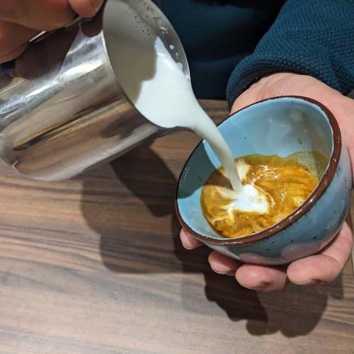 Eine Person gießt Milch in eine Tasse Kaffee