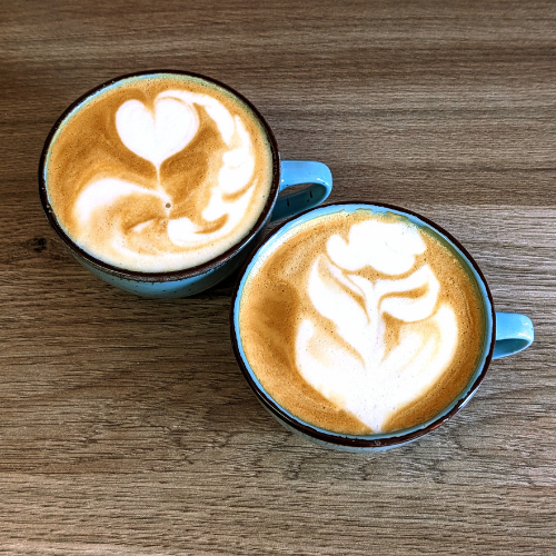 Zwei Tassen Cappuccino mit Latte Art auf einem Holztisch.