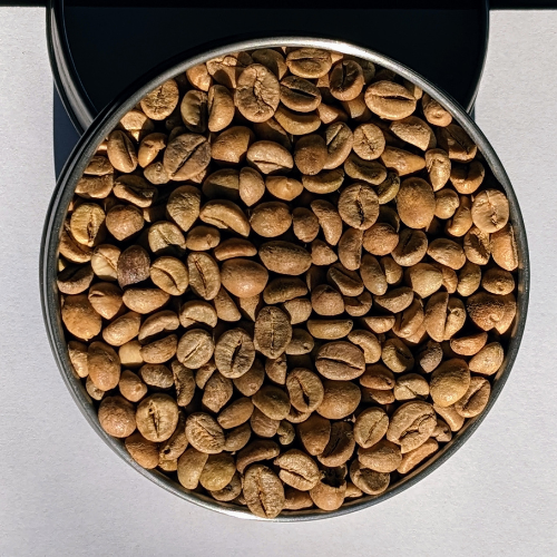 Eine mit Kaffeebohnen gefüllte Metallschüssel auf einer weißen Oberfläche