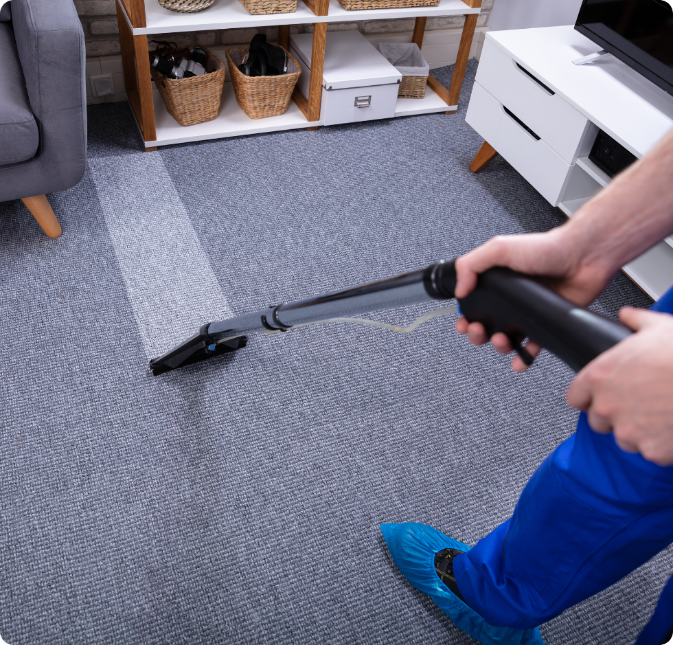 Une personne passe l'aspirateur sur une moquette grise dans un salon avec un aspirateur portatif.