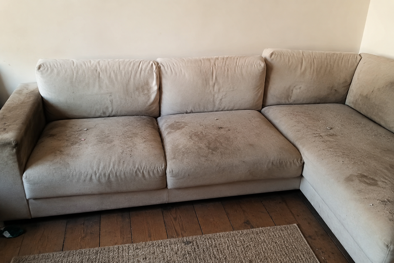 Canapé d'angle beige en forme de L avec coussins, dans un salon adossé à un mur clair.