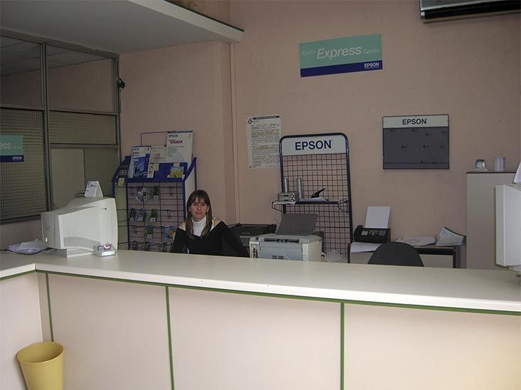 Una mujer se sienta en un escritorio frente a un cartel de Epson.