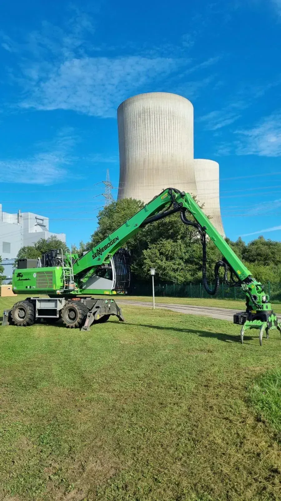 Ein grüner Kran steht auf einer Wiese vor einem Kühlturm.