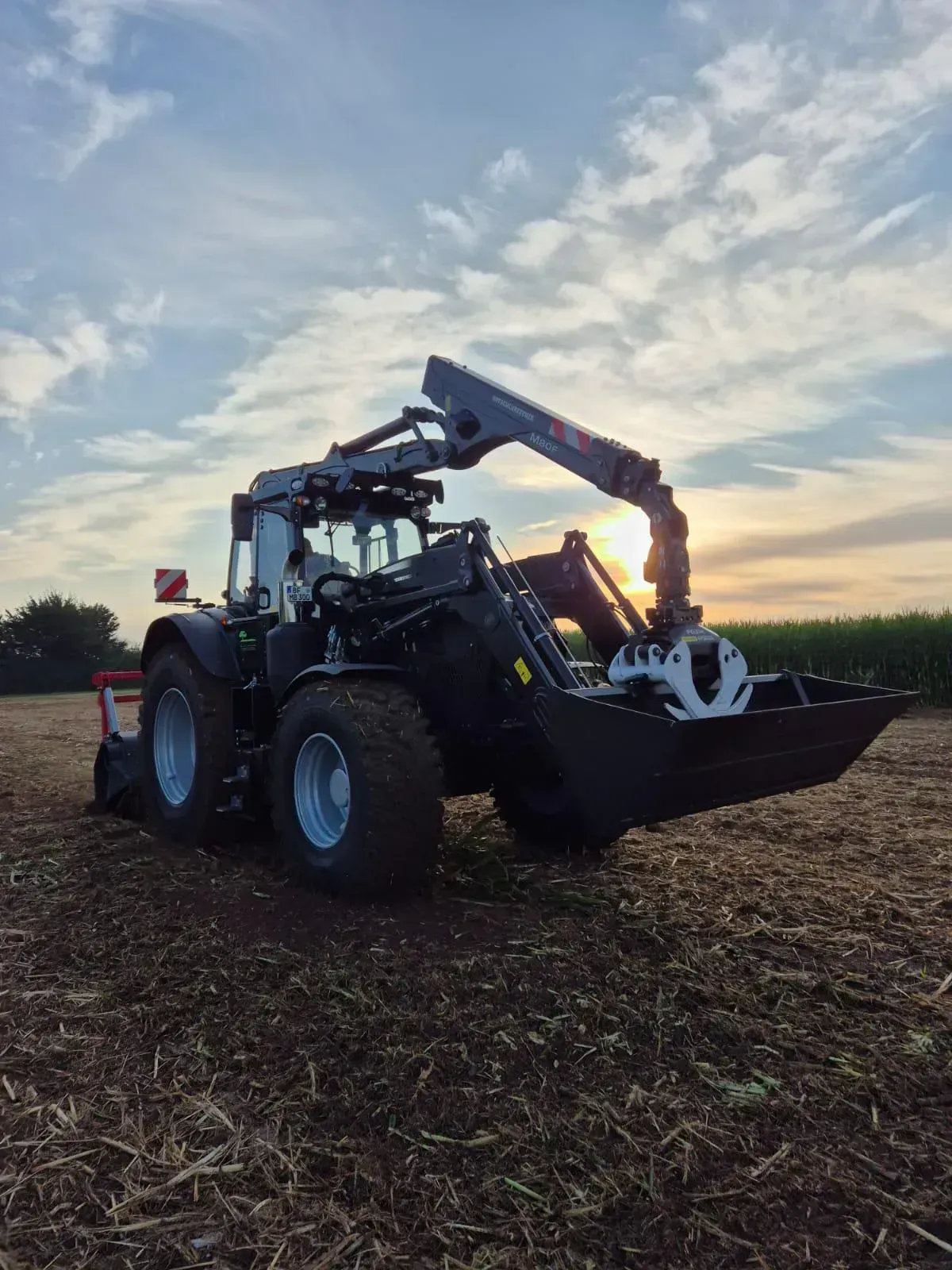 Auf einem Feld steht ein Traktor mit einem daran befestigten Kran.