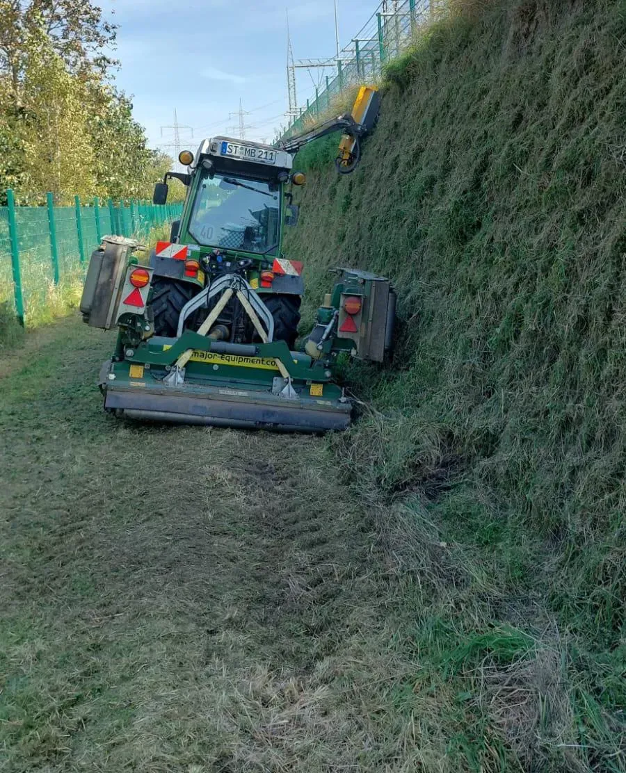 Ein grüner Traktor mäht Gras an einem Hang.