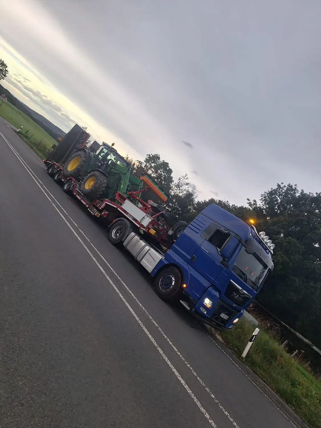 Ein blauer Lastwagen fährt mit Traktoren beladen eine Straße entlang.