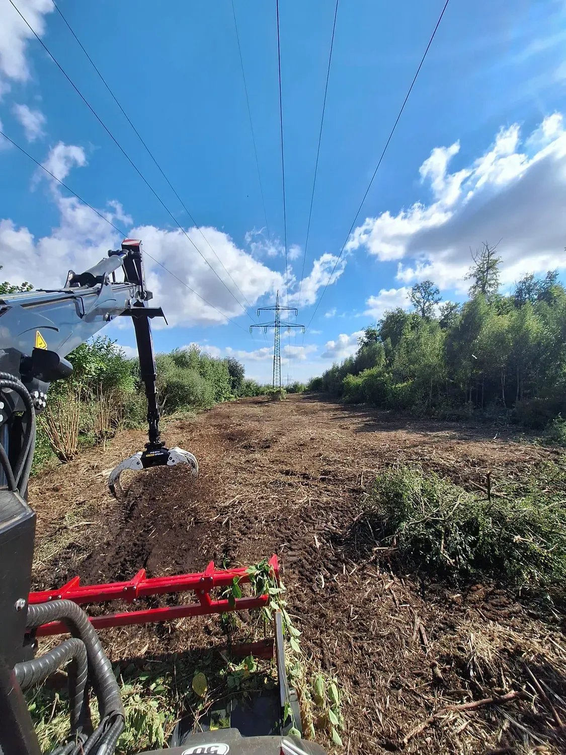 Ein Traktor fährt auf einer unbefestigten Straße neben Stromleitungen entlang.