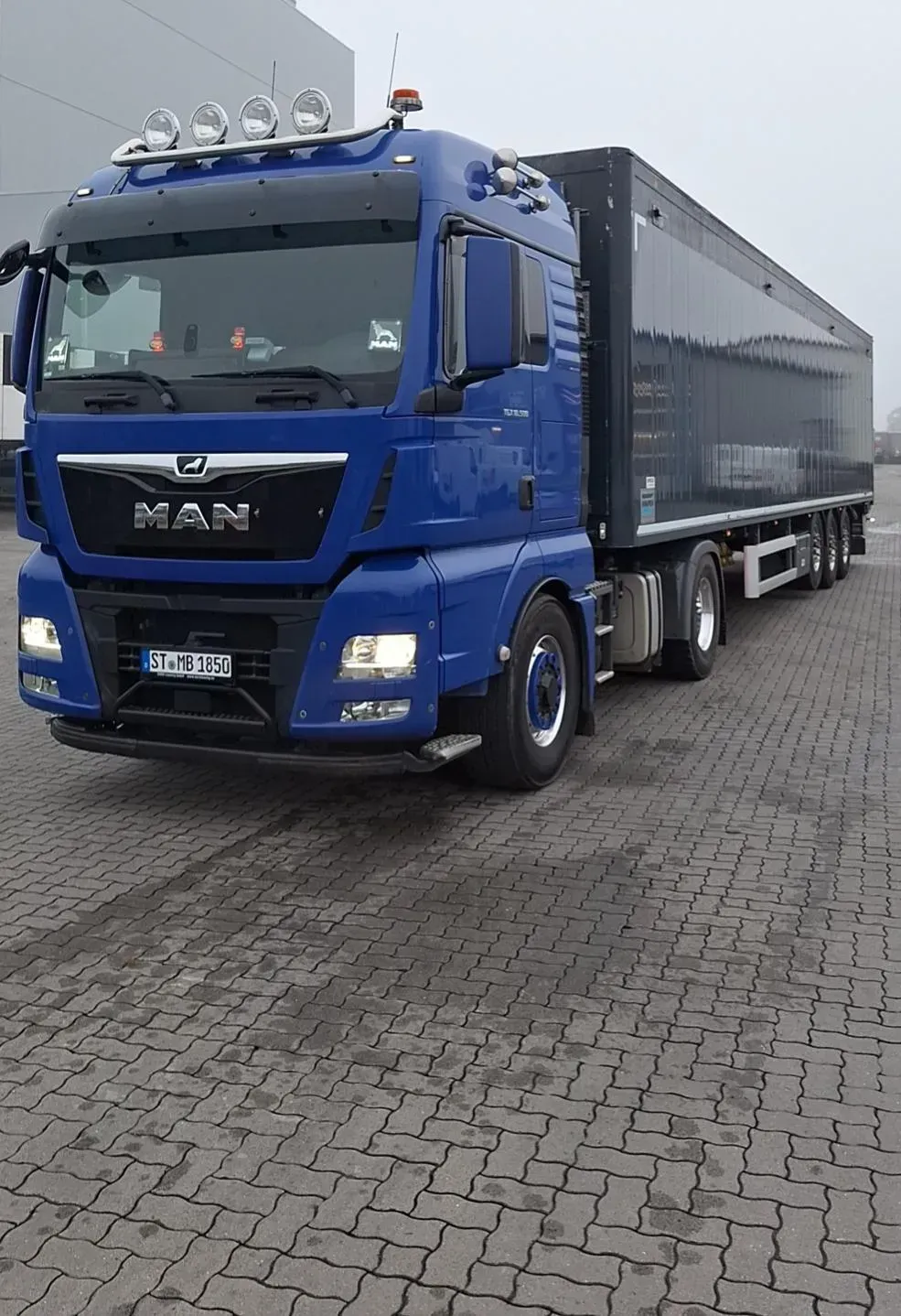 Ein blauer Lastwagen ist auf einer Ziegelsteinstraße geparkt.