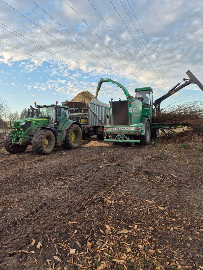 Ein John Deere-Traktor belädt einen Anhänger mit Holzspänen.