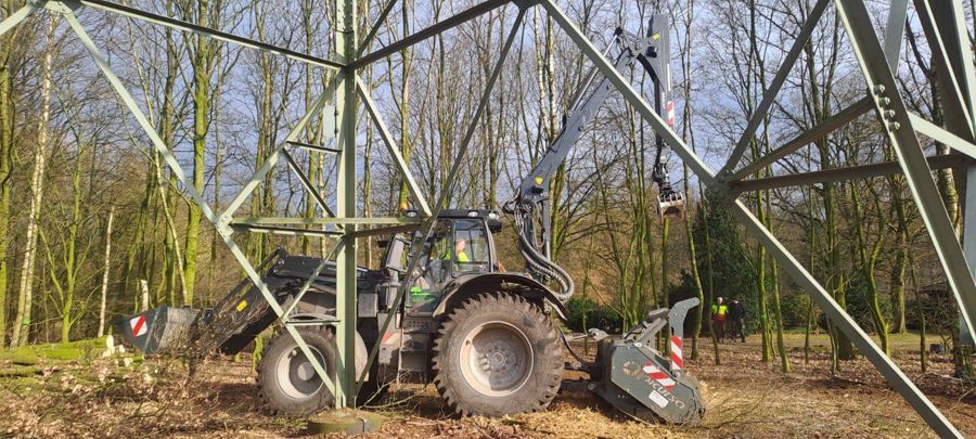 Ein Traktor steht mitten im Wald neben einem Strommast.