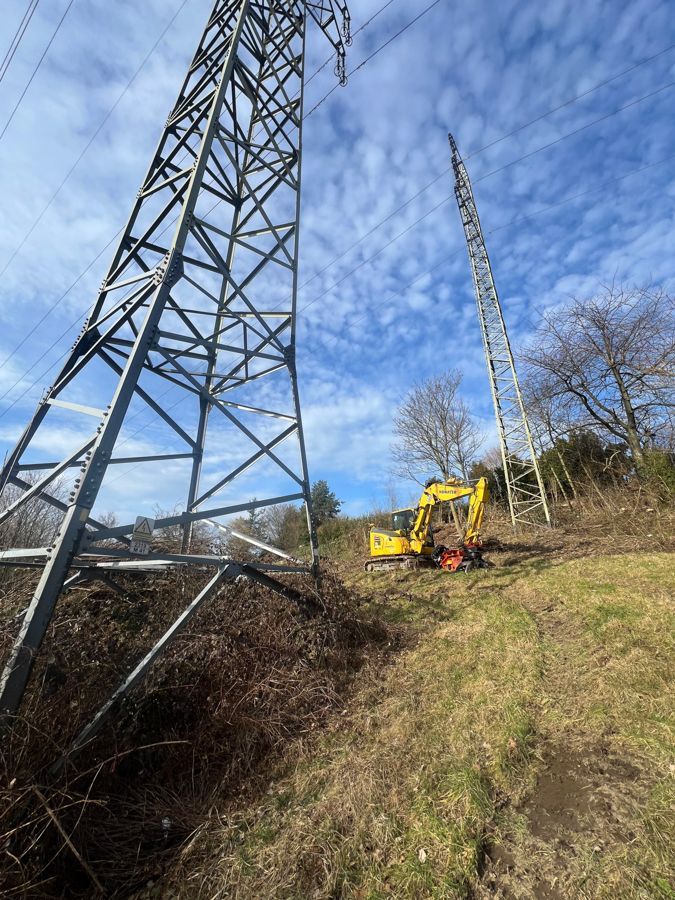 Ein gelber Bagger steht neben einem Strommast auf einem Feld.