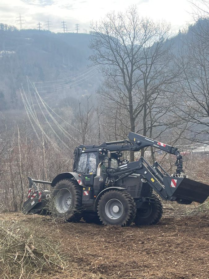Ein Traktor fährt auf einem Feldweg neben einem Bahngleis entlang.