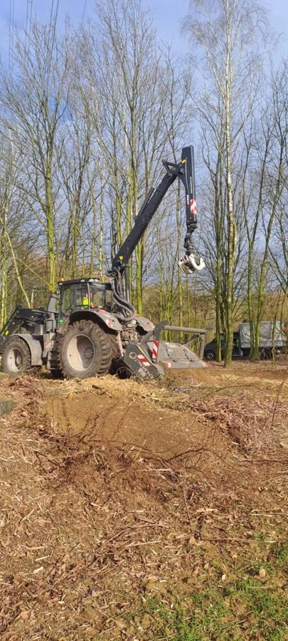 Ein Traktor mit einem daran befestigten Kran fährt durch ein Feld.