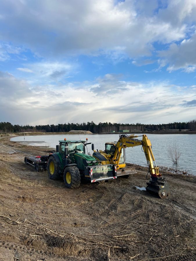 Ein Traktor und ein Bagger stehen am Ufer eines Sees.